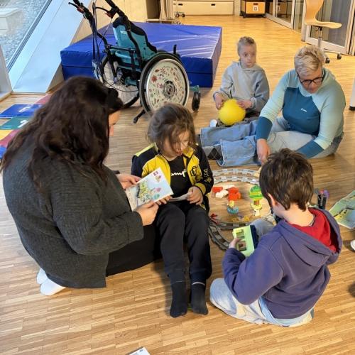 Kinder und Erwachsene sitzen am Boden und spielen mit einem Zug