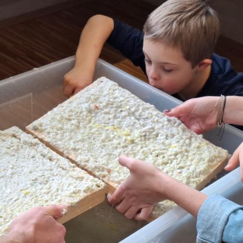 Papier schöpfen, man sieht Hände und das Kind über die Box schauen