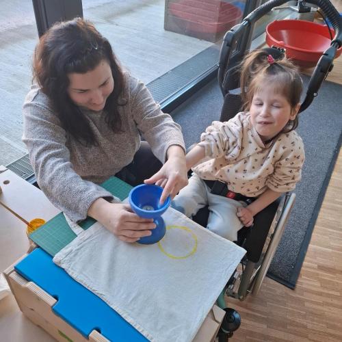 Kind im Rollstuhl stempelt mit Hilfe auf einen Stoffbeutel