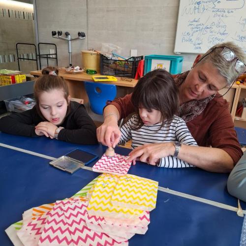 Kind stempelt das Schullogo mit Hilfe auf bunte Säckchen