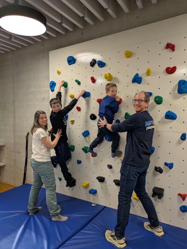 2 Kinder klettern die Kletterwand hinauf, 2 Erwachsene stehen hinter ihnen