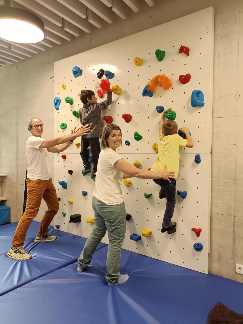 2 Kinder klettern die Kletterwand hinauf und werden von 2 Erwachsenen gesichert