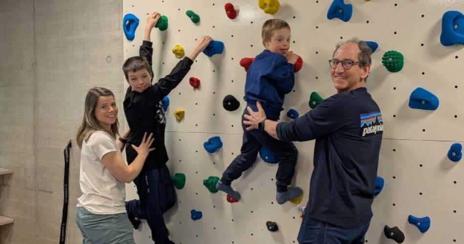 2 Kinder klettern die Kletterwand hinauf, 2 Erwachsene stehen hinter ihnen